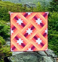 an orange and pink quilt is hanging on a rock