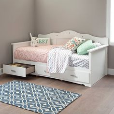 a white bed with drawers underneath it and a blue rug on the floor next to it