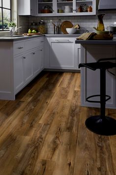 a kitchen with white cabinets and wood flooring on the counter top, along with a bar stool