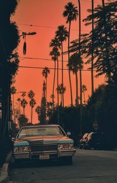 an old car is parked on the side of the road in front of palm trees