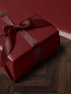 a red gift box with a large bow on it's side sitting on a wooden floor