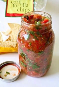 a jar filled with lots of food next to a bag of tortilla chips