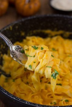 a spoon full of macaroni and cheese with parsley on the fork in a skillet