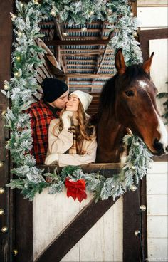 a man and woman are kissing in front of a christmas wreath with a horse behind them