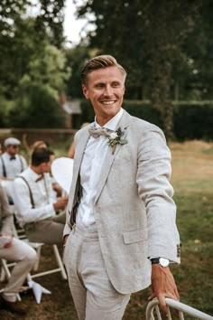 a man in a suit and bow tie standing next to other men sitting on lawn chairs