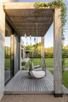 an outdoor swing chair sitting on top of a wooden deck under a pergolated roof