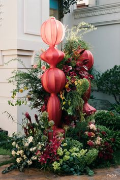 an arrangement of flowers and greenery is displayed in front of a building with red lanterns