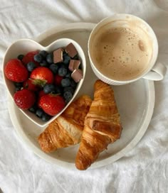 croissants, strawberries and coffee are on a plate with a heart shaped bowl