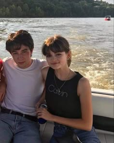 three young people sitting on the back of a boat in front of a body of water