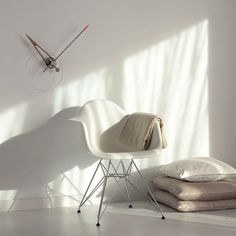 a white chair sitting in front of a clock on the wall next to pillows and blankets