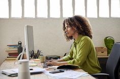 a woman sitting at a desk with a computer in front of her and looking off to the side