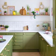 a kitchen with green cabinets and white counter tops, plants on the shelf above the sink