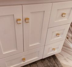 a white bathroom vanity with gold handles and knobs on the doors is shown in this image