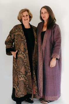 two women standing next to each other in front of a white wall and one is wearing a purple coat