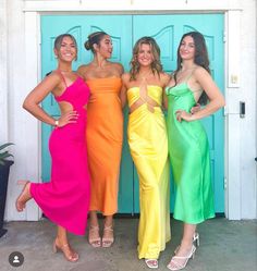 three beautiful women standing next to each other in front of a blue door wearing different colored dresses