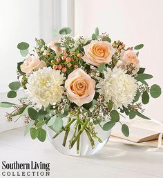 a vase filled with white flowers and greenery on top of a table next to an open book