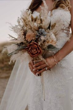 a woman in a wedding dress holding a bouquet with dried flowers and feathers on it