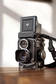 an old camera sitting on top of a wooden table next to a black strap and a white wall