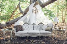 a white couch sitting under a tree next to a table