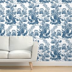 a white couch sitting in front of a blue and white wallpapered room with a wooden floor