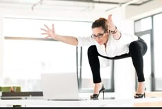 a woman in black pants and white shirt doing a handstand while using a laptop