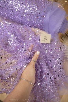 a hand is touching the sequins on a purple dress