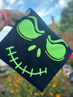 a person holding up a black square with neon green designs on it and an alien face painted on the side