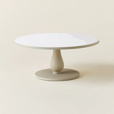 a white round table with an oval base on a plain surface, against a neutral background