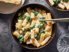 two bowls filled with pasta and spinach on top of a table