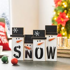 three snowmen with hats and carrots in front of a christmas tree on a table