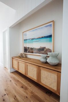 two white vases sitting on top of a wooden shelf in front of a painting