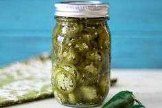 pickles in a glass jar on a table next to a cloth and green peppers