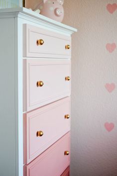 a white dresser with pink drawers and hearts painted on the wall in a child's bedroom