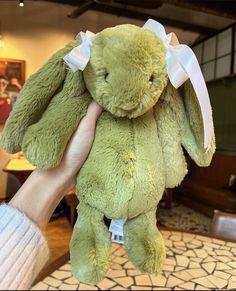 a hand holding a green stuffed animal with a white bow on it's head