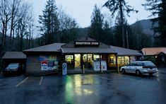 an empty parking lot with cars parked in front of it and the storefront is lit up at night