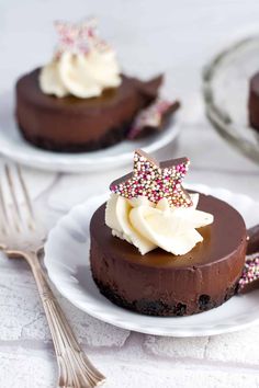 two white plates topped with chocolate cheesecake covered in whipped cream and sprinkles