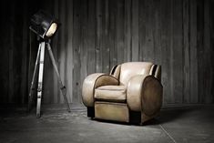 a chair with a light on it sitting in front of a wooden wall next to a floor lamp