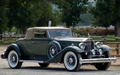 an antique car is parked on the side of the road in front of some trees