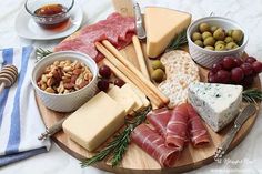 an assortment of cheeses and meats on a wooden platter with olives