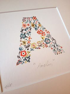 the letter a is made up of flowers and leaves on white paper with writing underneath it