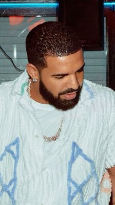 a man with a beard wearing a white sweater and blue letters on his shirt is looking down