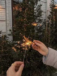 two people holding sparklers in front of a christmas tree with lights on the branches