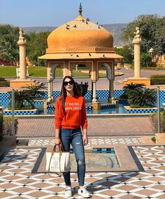 a woman standing in front of a gazebo holding a white purse and wearing an orange shirt