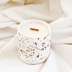 a white candle sitting on top of a bed covered in white sheets and fabric with a wooden stick sticking out of it's center