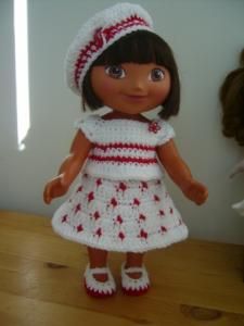 a crocheted doll wearing a white dress and red hat on top of a wooden table