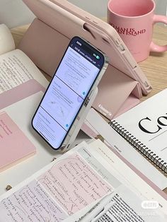 a cell phone sitting on top of an open book next to a notebook and coffee cup