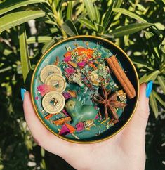 a person holding a bowl filled with spices and other items in their hands, surrounded by plants