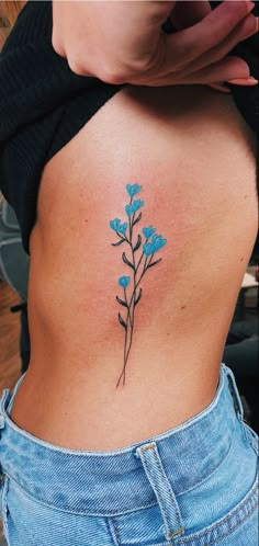 a woman's lower back tattoo with blue flowers on her left side ribcage