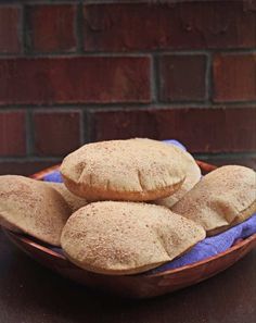 a wooden bowl filled with bread on top of a purple cloth next to a brick wall