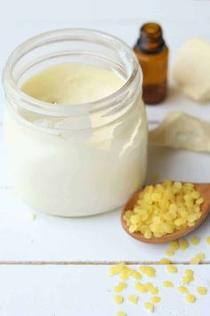 a wooden spoon filled with corn kernels next to a jar of cream and some other ingredients